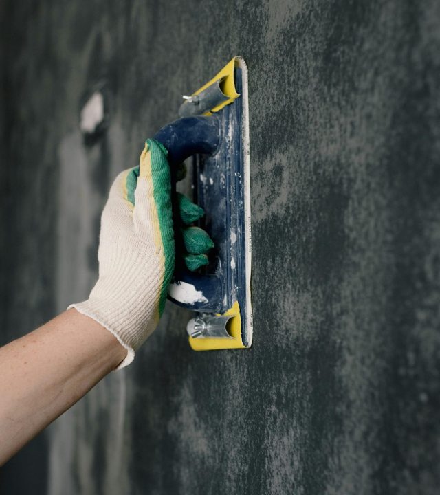 Crop anonymous male worker in gloves holding scraper and aligning walls in flat