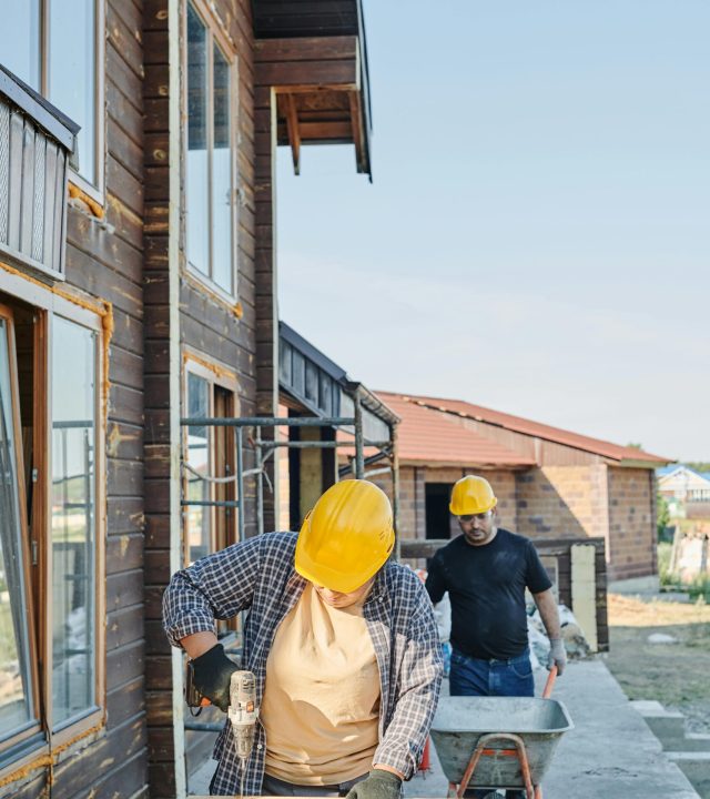 Two workers in hard hats engaged in carpentry at a construction site, building a wooden house.